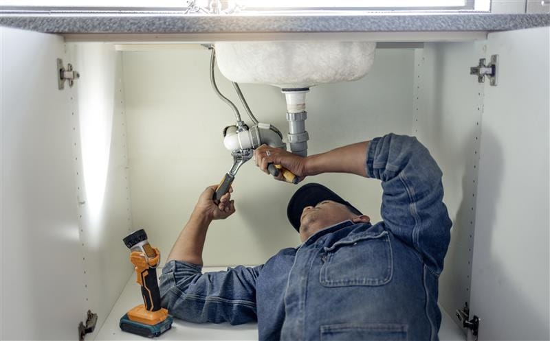 Plumber repairing pipes beneath a bathroom sink in Covina
